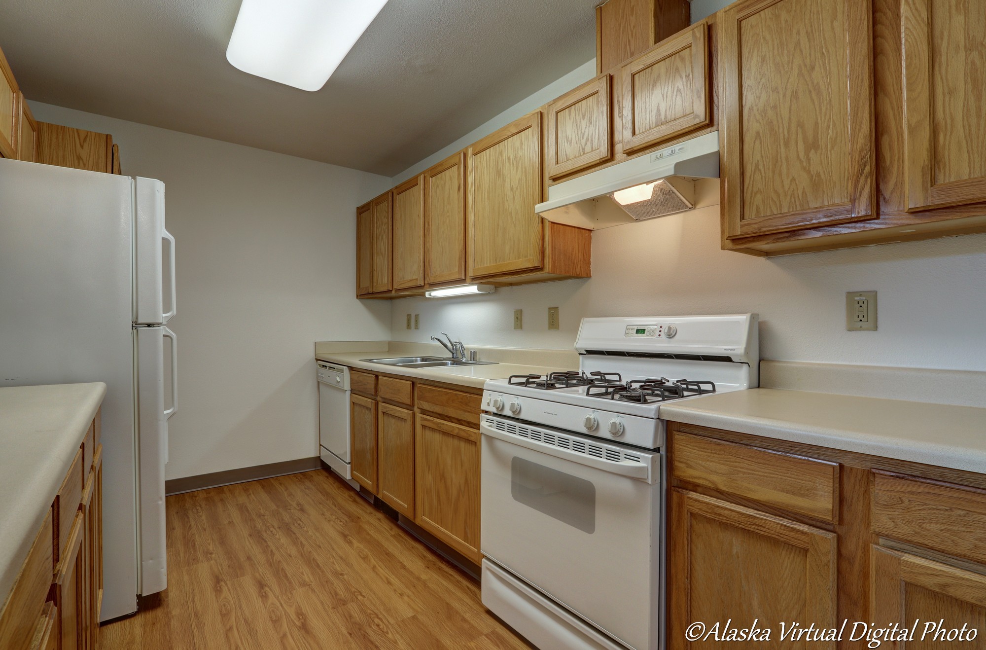 image of kitchen with wooden cabinets, wooden floors, and tan countertops.