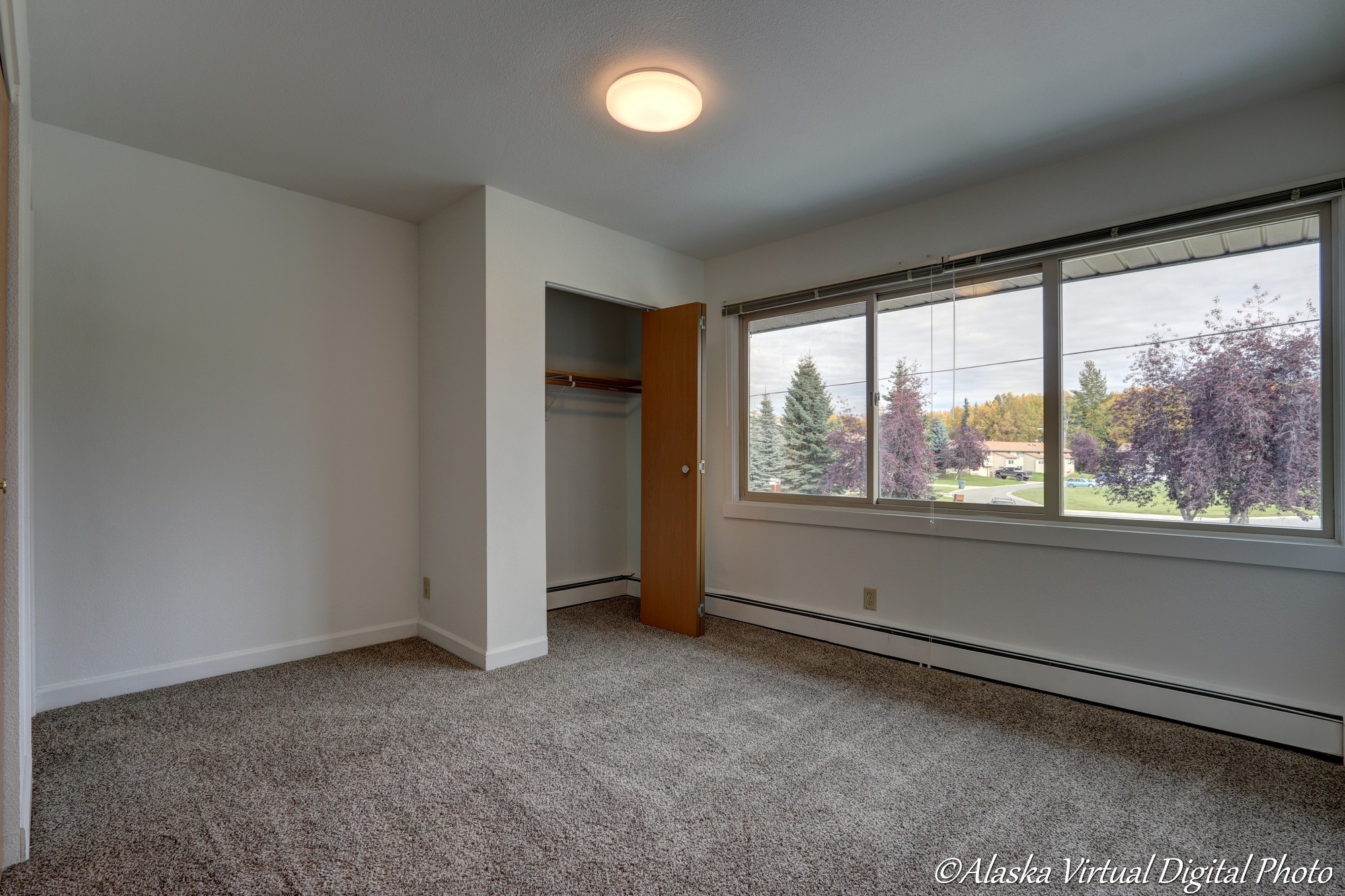 Image of bedroom with 3 windows overlooking the neighborhood. Trees with fall colors in the background