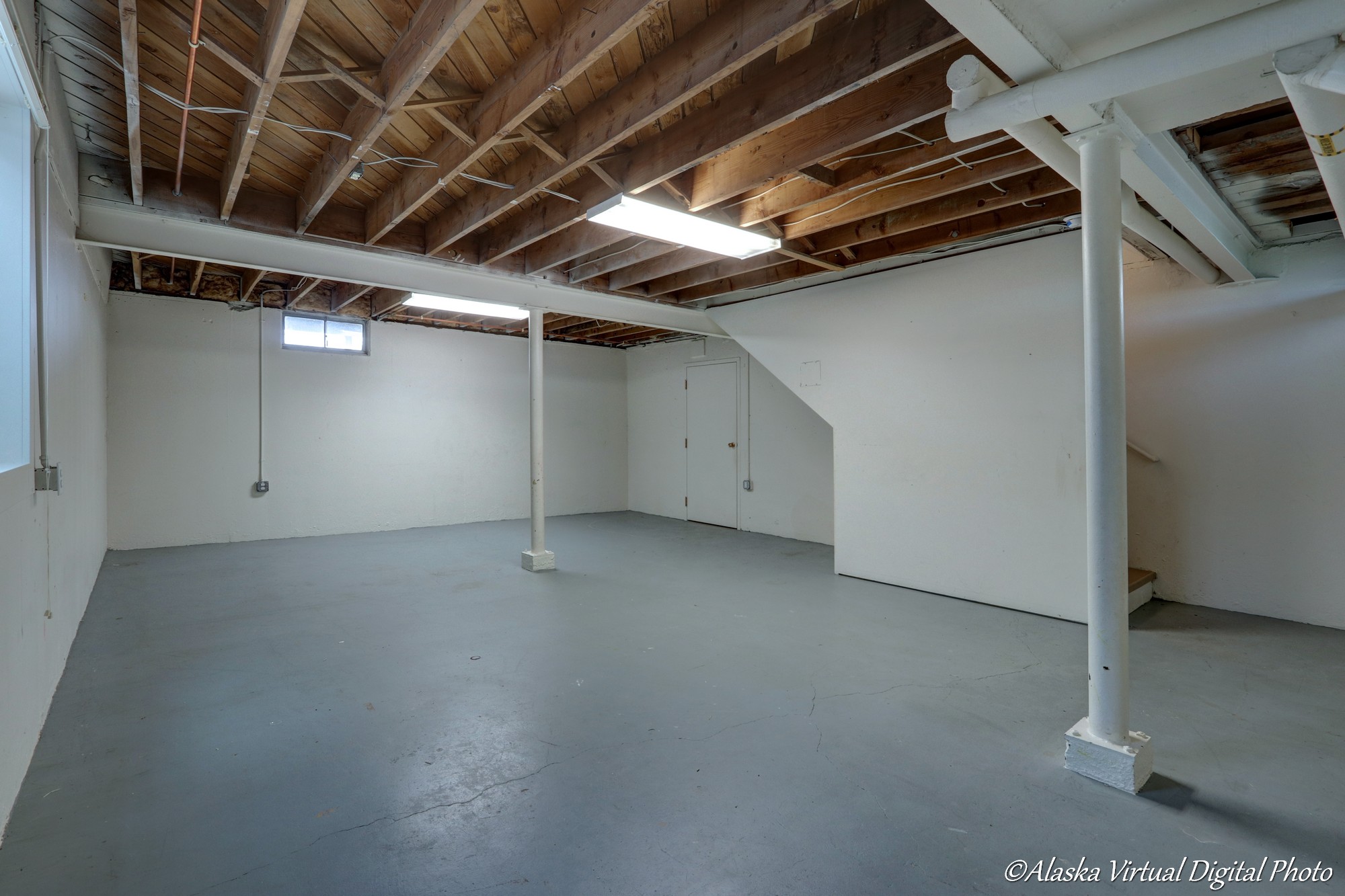 Unfinished basement with blue floor and exposed beams