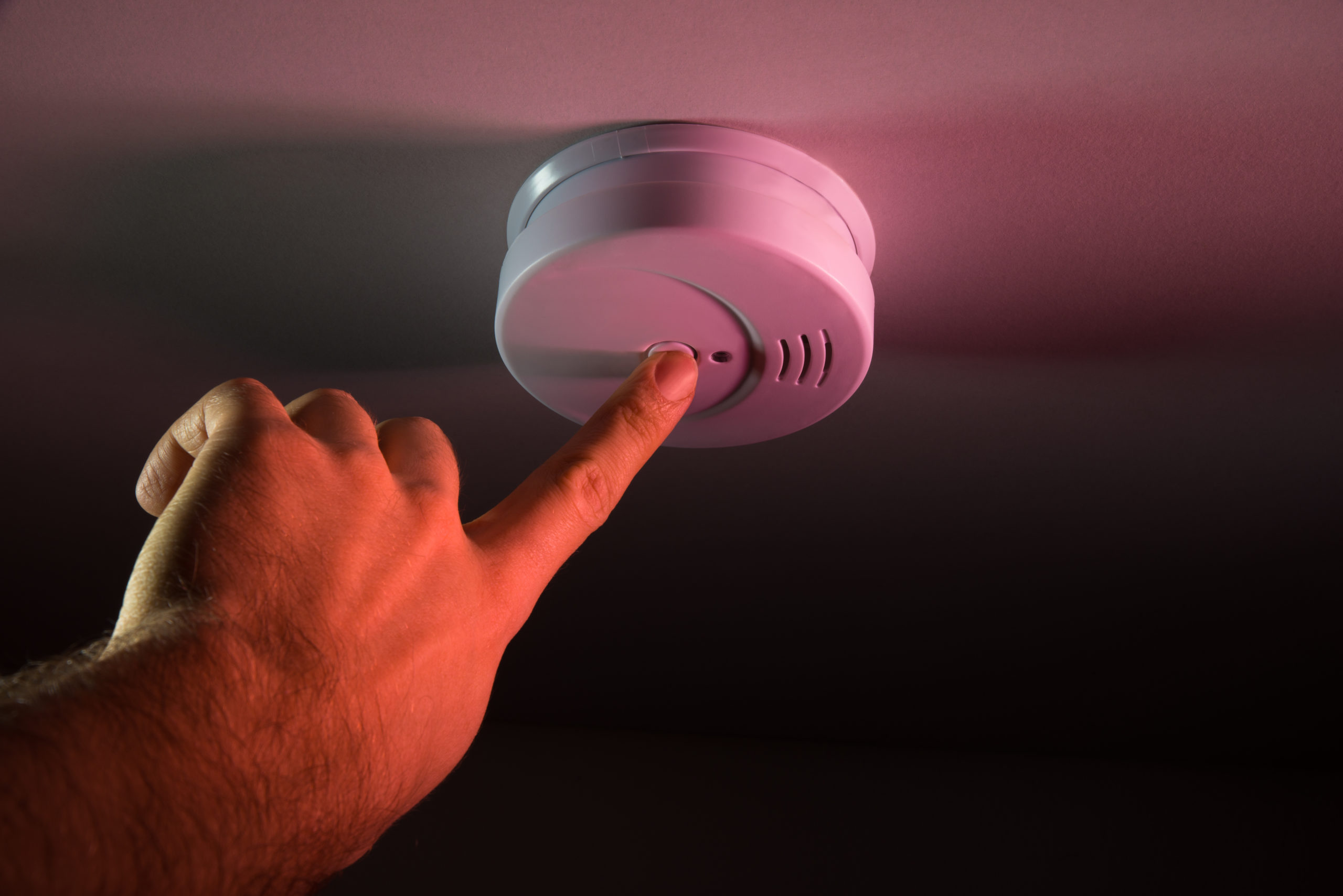 Close-up Of Person Hand Pressing Smoke Detector