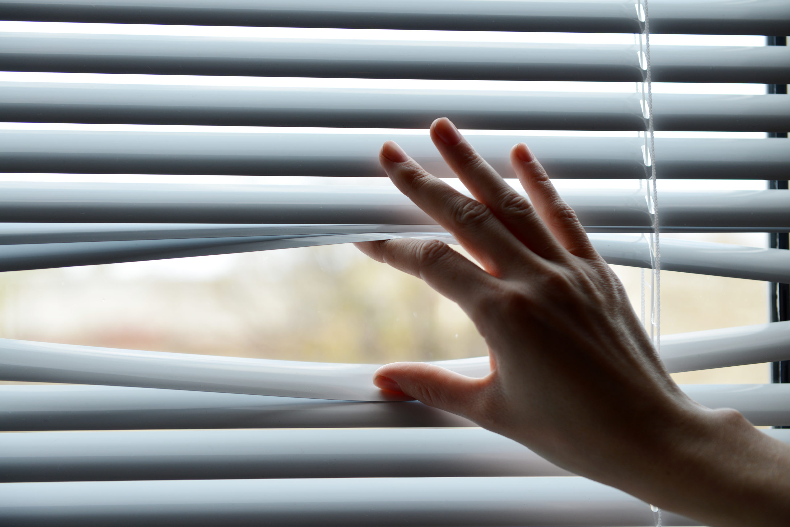 Female hand separating slats of venetian blinds with a finger to see through