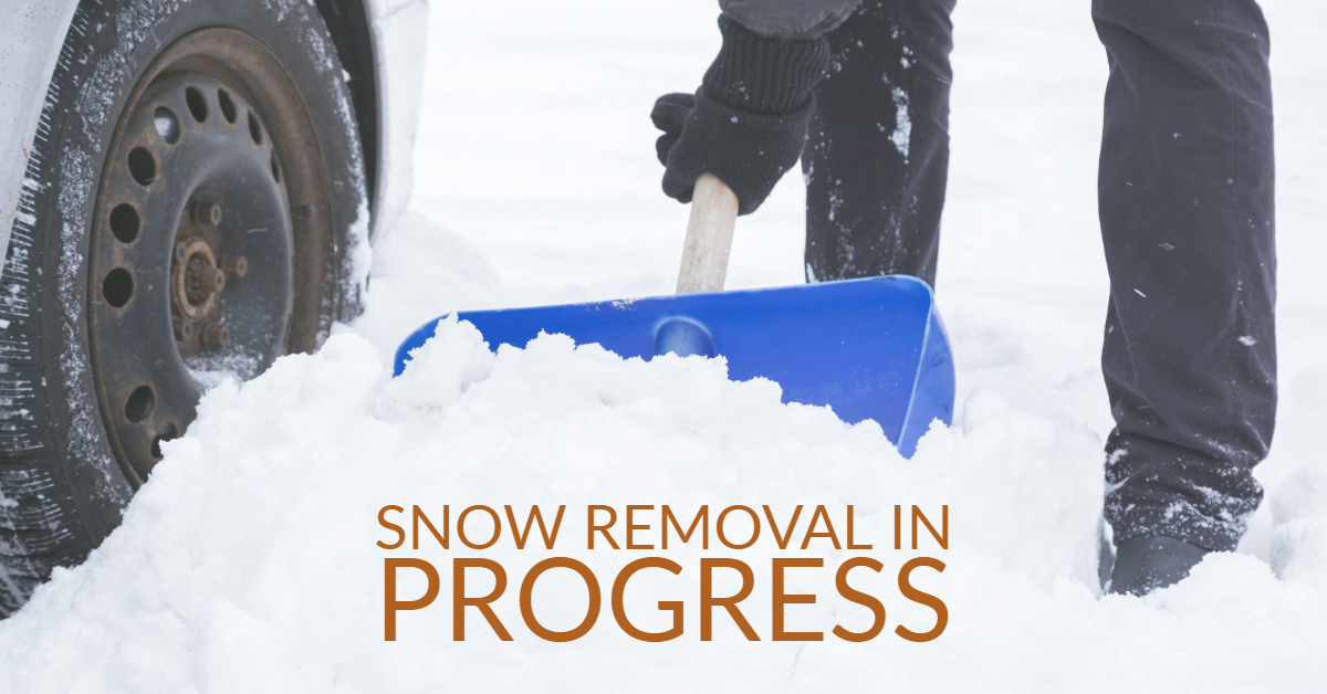 Man with blue shovel removing snow front of car wheel in winter day