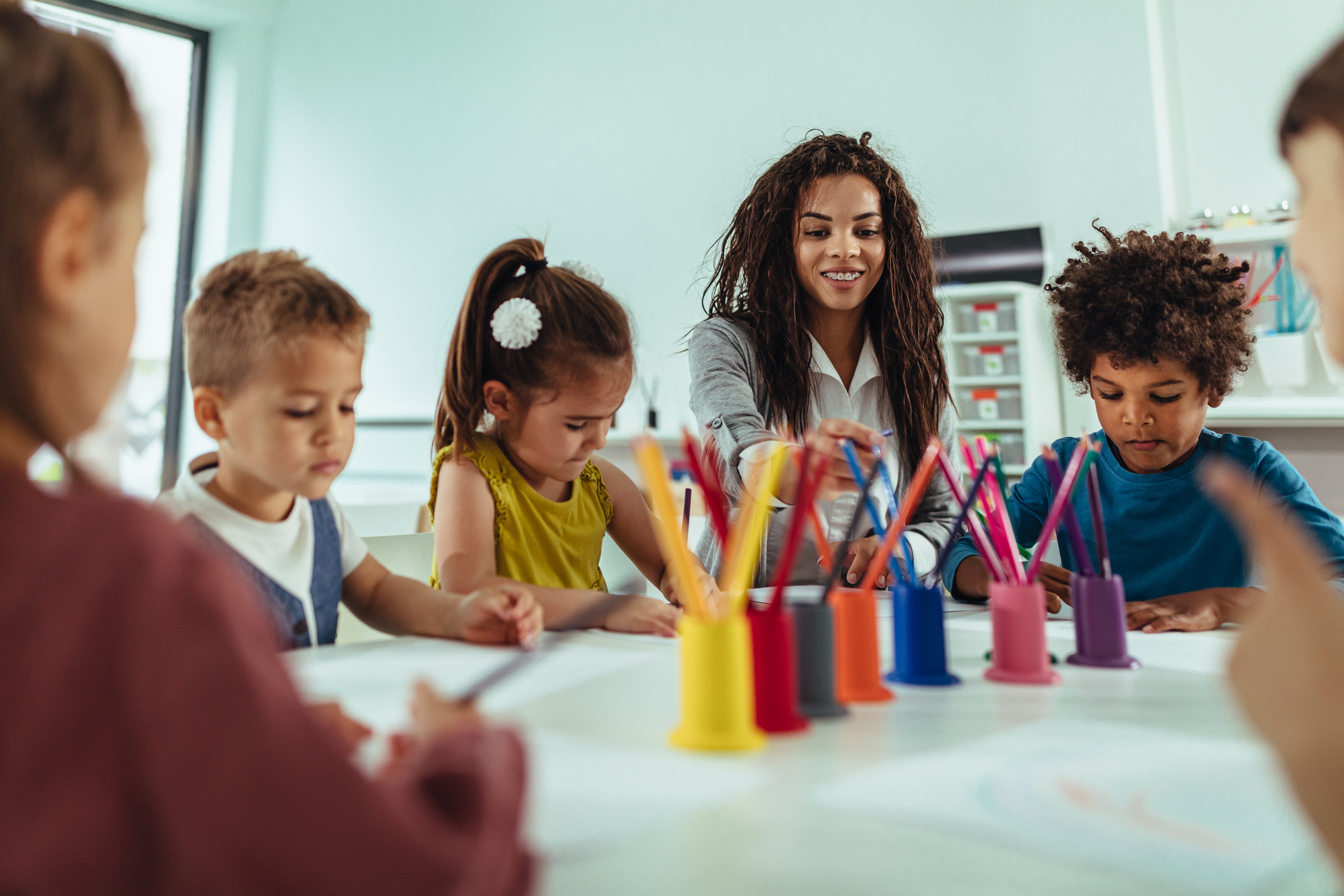 Teacher and adorable children being creative with colorful pencils at kindergarten