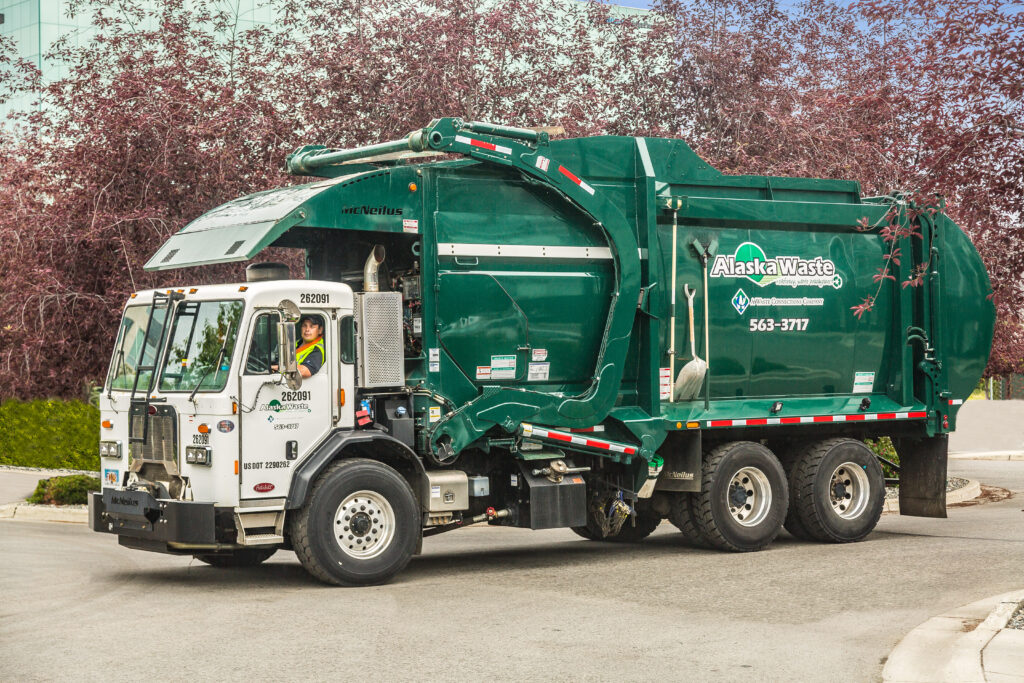 Green Trash truck with backdrop of trees